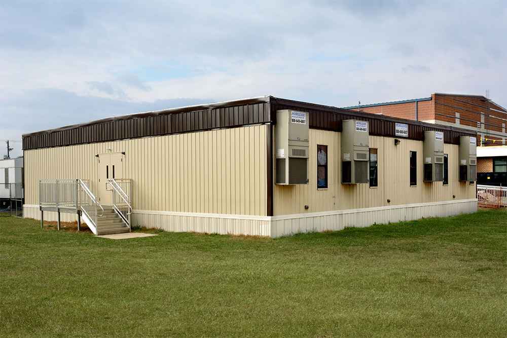 Side view of a modular building with multiple HVAC units and dual-door entry on grassy field in USA