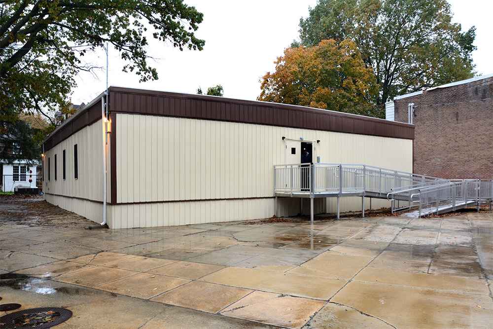 Large modular classroom structure with HVAC units and ramp access next to school playground in USA