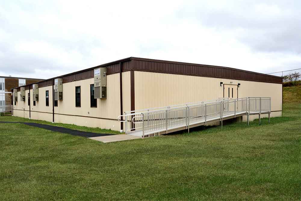 Side view of a modular building with multiple HVAC units and door entry on grassy field in USA