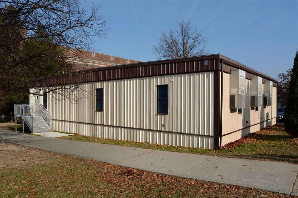Large modular classroom structure with HVAC units and ramp access next to school playground in USA